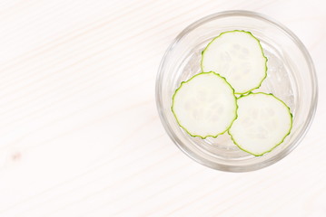 A glass of water with three slices of fresh cucumber on a light