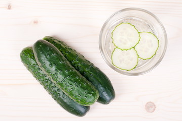 A glass of water with three slices of fresh cucumber, next to th