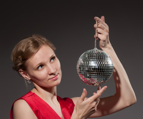 Young woman holding disco ball sitting on grey background