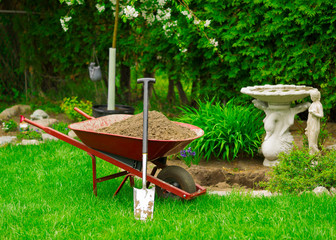 Wheelbarrow Full of Dirt with Leaning Shovel in Garden