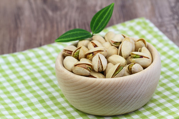 Pistachio nuts in wooden bowl on checkered cloth
