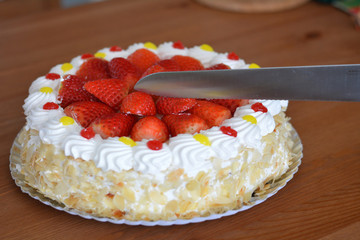 Female hand cutting cream cake with almond.