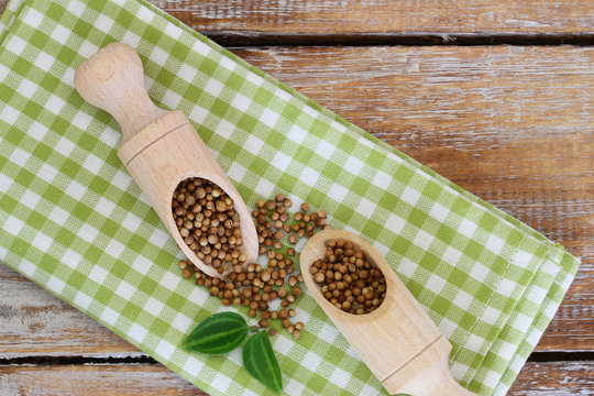 Coriander seeds on wooden scoops on checkered cloth
