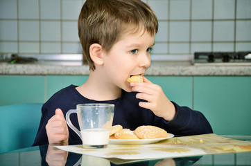 little boy bites cookies, sitting at the dinner table.  horizont