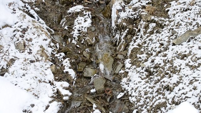 Small mountain brook flowing on stony snowy soil in winter