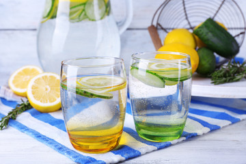 Fresh water with lemon and cucumber in glassware on wooden table, closeup
