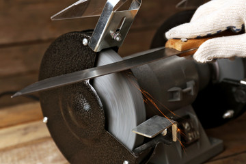 Knife sharpener and hand with blade on wooden table, closeup