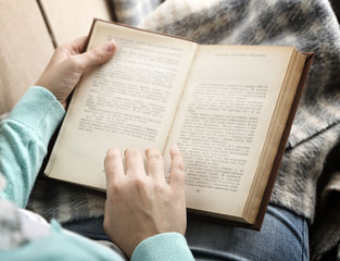 Young woman reading book, close-up, on home interior background