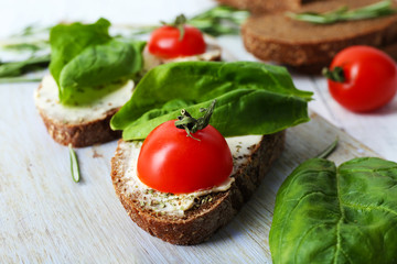 Delicious sandwiches with tomatoes and greens on cutting board on table close up