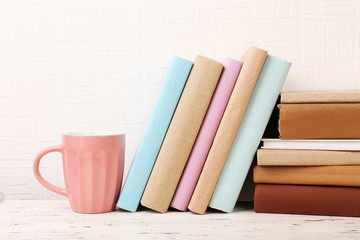 Fototapeta na wymiar Books and cup on wooden shelf on wallpaper background