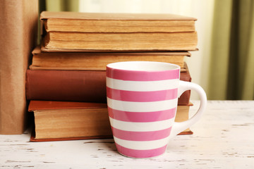 Books and cup on wooden table, on curtains background