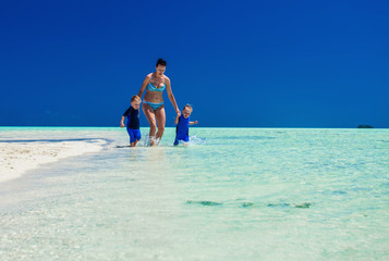 Two boys running with mother on a tropical bach