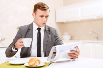 Businessman drinking with croissant coffee and reading newspaper
