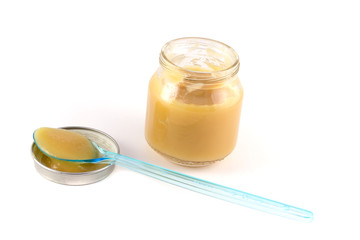 Baby fruit puree in the pot with a plastic spoon