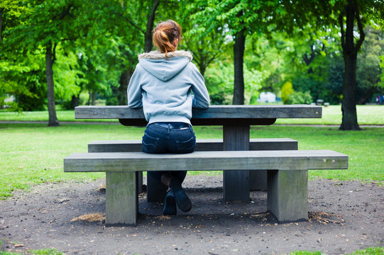 Young woman sitting on bench by table in park