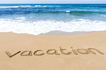 word vacation written on sandy beach at sea