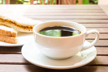 Black coffee served with sandwich bread at the background
