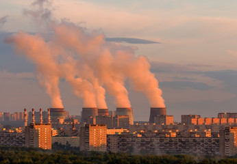 Cooling tower power plant with steam on a background of the city at sunset