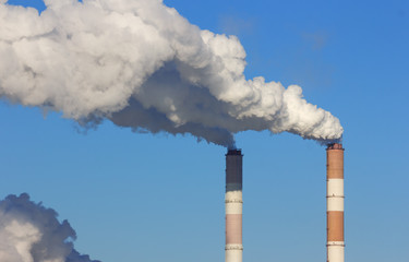 Pipes of thermal power plant with white smoke against the blue sky