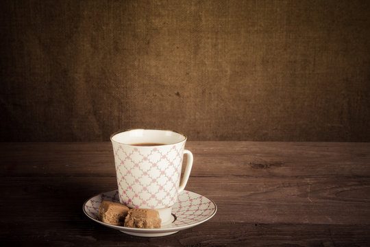Porcelain cup of coffee with toffee on old wooden table against