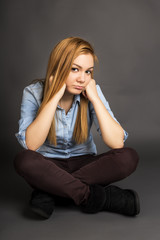 Sulky teenage girl sitting on the floor with legs crossed - obrazy, fototapety, plakaty