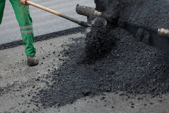 workman with shovel working on new asphalt
