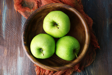Green apples in bowl with fabric on wooden table, top view