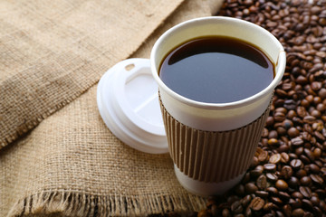 Paper cup of coffee with beans on sackcloth close up