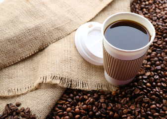 Paper cup of coffee with beans on sackcloth close up