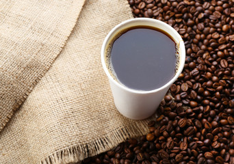 Paper cup of coffee with beans on sackcloth close up