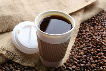 Paper cup of coffee with beans on sackcloth close up
