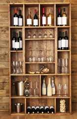 Shelving with wine bottles with glasses on wooden wall background