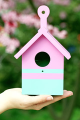 Obraz na płótnie Canvas Decorative nesting box in female hands on blooming garden background