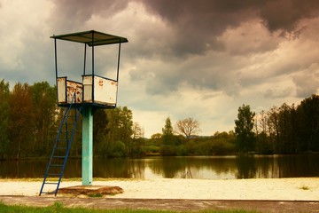An old white and rusty metal lifeguard with chair on pond beach.