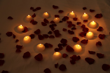 Heart of candles and red petals on bed, close up