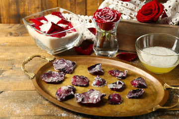 Making candied rose flower petals with egg whites and sugar, on wooden background