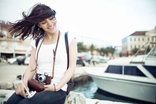 Summer beach woman fun holding vintage retro camera laughing and smiling happy during summer holiday vacation travel.Women sitting on sea deck near marine boat in island Korcula Croatia