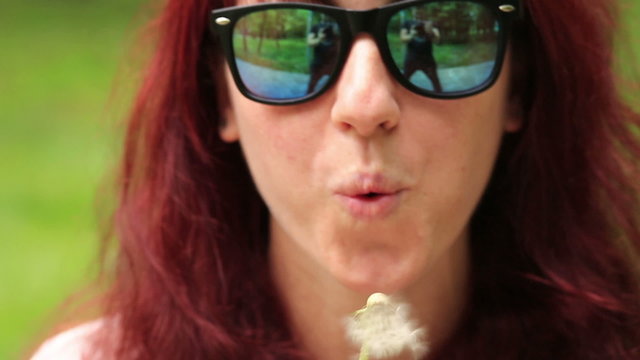 Beautiful woman blows dandelion seeds to the camera