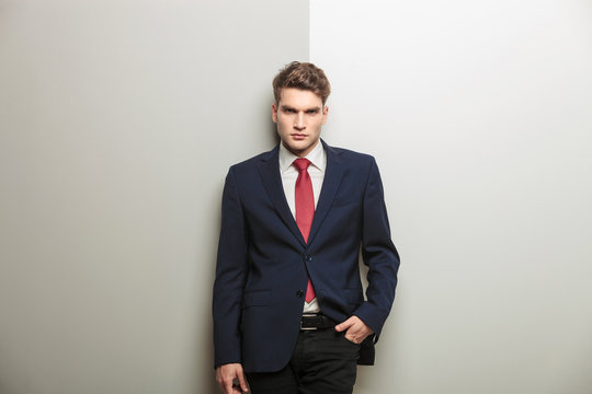Casual young business man leaning on a grey wall.