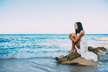 beautiful girl sitting on a rock on the beach sea