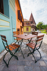 Table with chairs on stone paved old street and colored houses f