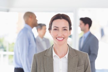 Businesswoman smiling at camera while her colleagues discussing 