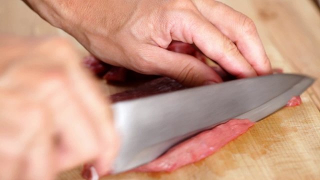 Chef finely slicing beef steak onto small chunks; closeup