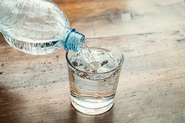 Foto op Plexiglas blue water bottle poured into a clear glass © GianlucaCiroTancredi