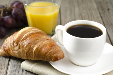 cup of coffee on a wooden tbale with juice, croissant, grapes