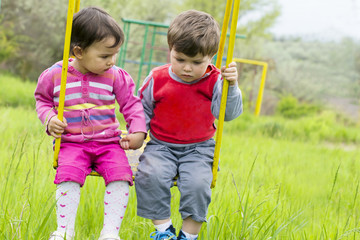 Two little kids having fun on a swing on summer day