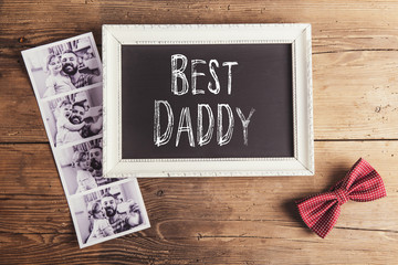 Picture frame, polaroid photos and bow tie on wooden background.