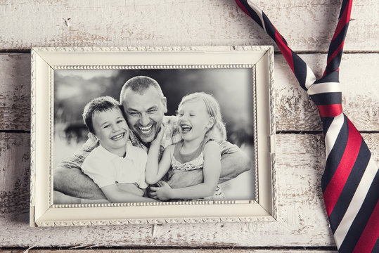 Picture frame with family photo and a tie on wooden background.