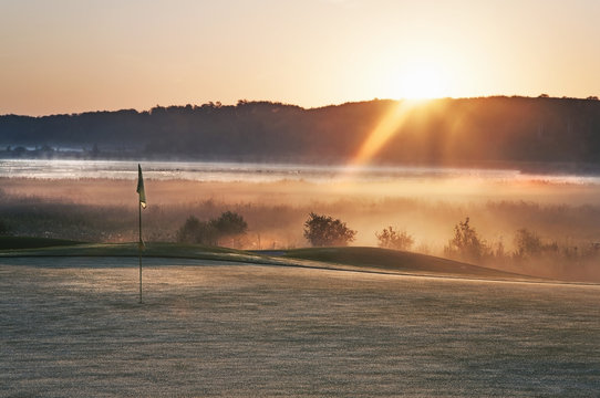 Glowing dawn light on a golf course green. The sun just appearing above a mountain range.