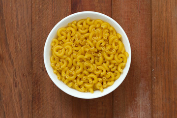 dry pasta in white bowl on brown wooden background